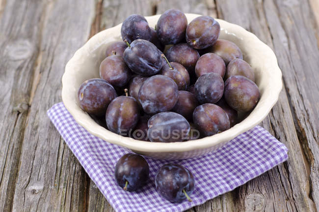 Bowl of plums with napkin on wooden table — Stock Photo