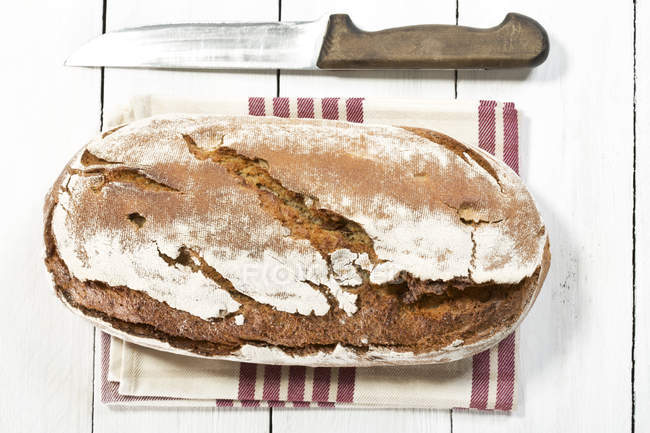Frisch gebackener Brotlaib auf Küchentuch mit Messer — Stockfoto