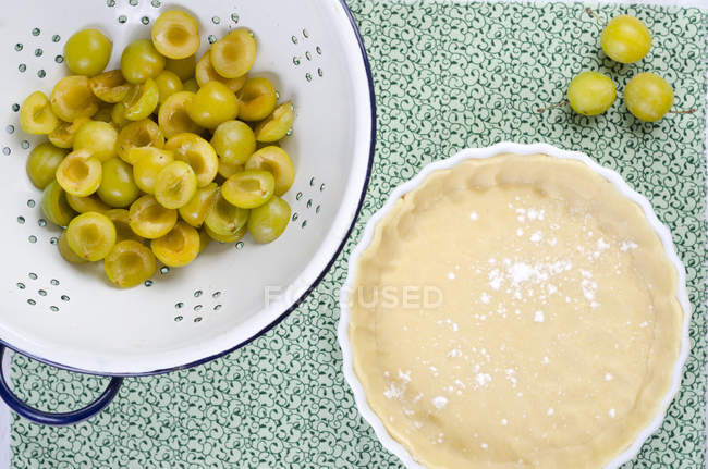 Pâtisserie courte crue dans un plat de cuisson et passoire avec mirabelles sur une table — Photo de stock