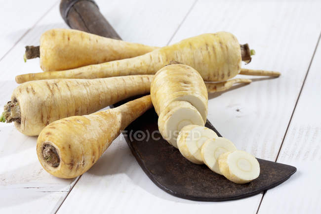 Sliced and whole parsnips with antique knife on white wooden table — Stock Photo