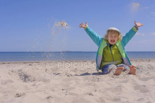 Boy sitting at beach throwing sand — Stock Photo