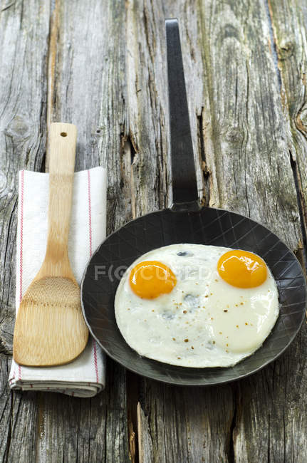Fried eggs in pan with wooden spoon on napkin — Stock Photo