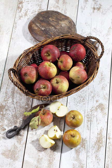 Bio-Äpfel im Korb, Holzschaufel und Vintage-Messer auf weißem Holztisch — Stockfoto