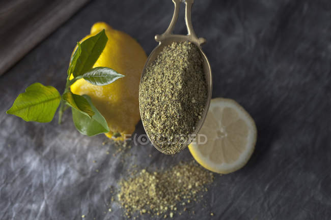Paleta de latón con pimienta de limón seca granulada con limón fresco y hojas en tela negra - foto de stock