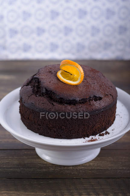 Chocolate cake garnished with orange slice on cake stand on wooden table — Stock Photo
