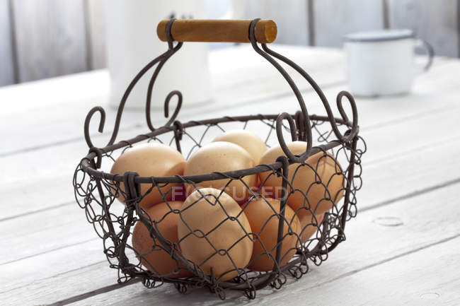 Fresh eggs in wire basket on wooden table — Stock Photo