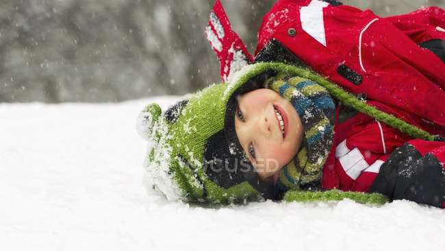 Ritratto di ragazzo sdraiato sulla neve in inverno e guardando la macchina fotografica — Foto stock