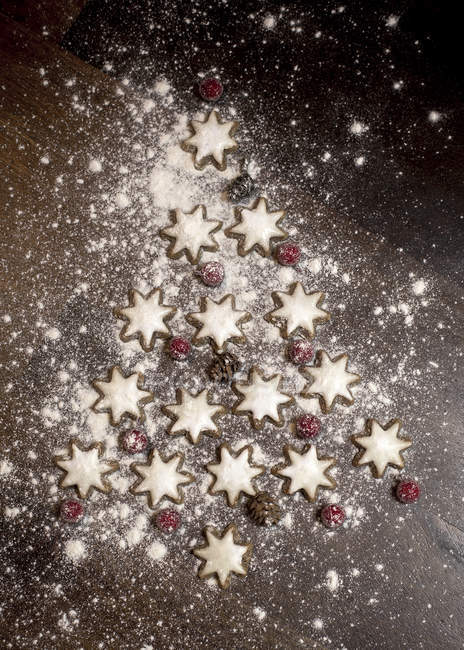 Albero di Natale formato da biscotti alla cannella a forma di stella, bacche rosse e coni di abete su tavolo di legno — Foto stock