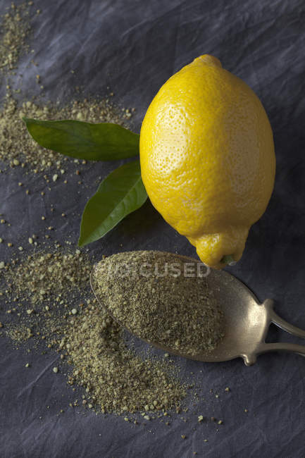 Truelle en laiton avec du poivre de citron sec grainé avec du citron frais et des feuilles sur tissu noir — Photo de stock