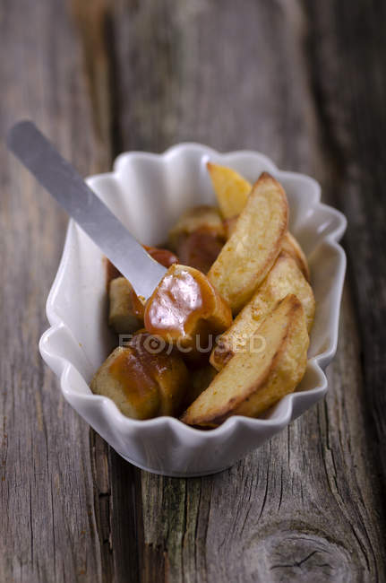 Ковбаса на грилі з соусом каррі та картопляними клинами — стокове фото