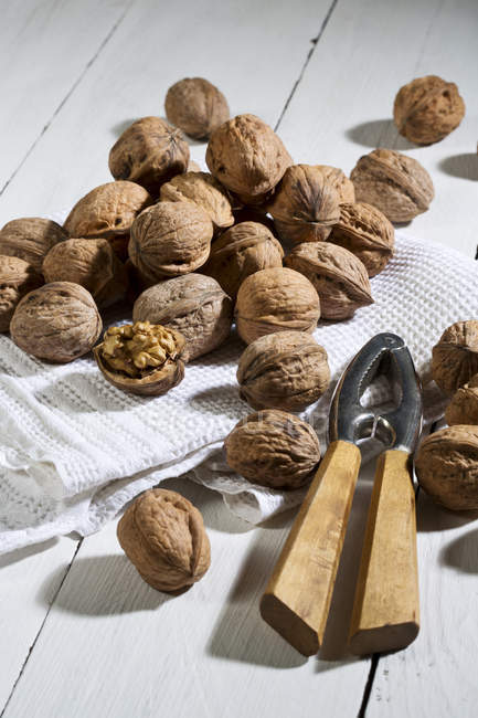Whole and cracked Walnuts with nutcracker and dish towel on white wooden table — Stock Photo