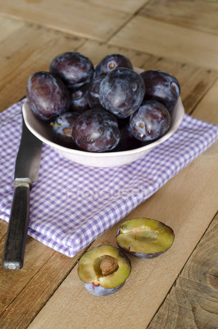 Fresh plums in bowl on checkered cloth with knife — Stock Photo