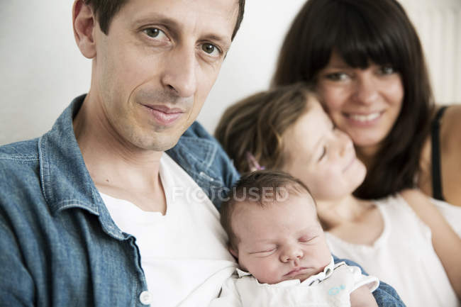 Jovens pais com recém-nascido do sexo masculino e pequena filha sentada no sofá em casa — Fotografia de Stock