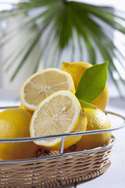Primer plano de limones frescos enteros y cortados a la mitad en la cesta - foto de stock