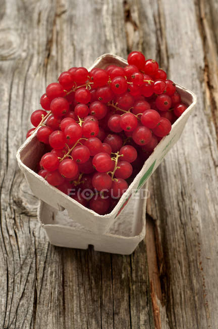 Grosellas rojas frescas en caja de cartón sobre madera - foto de stock