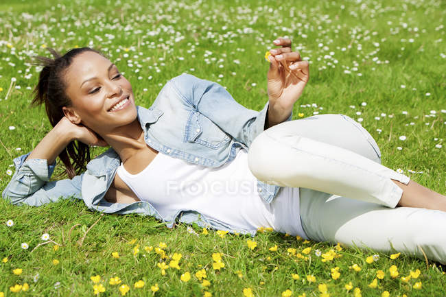 Sonriente mujer joven acostada en el prado de flores - foto de stock