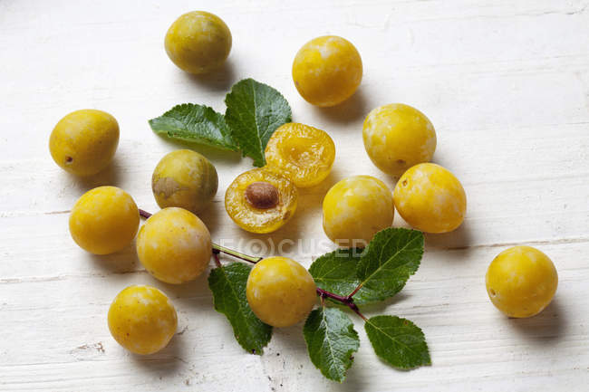 Whole and halved mirabelle plums on white wooden surface — Stock Photo