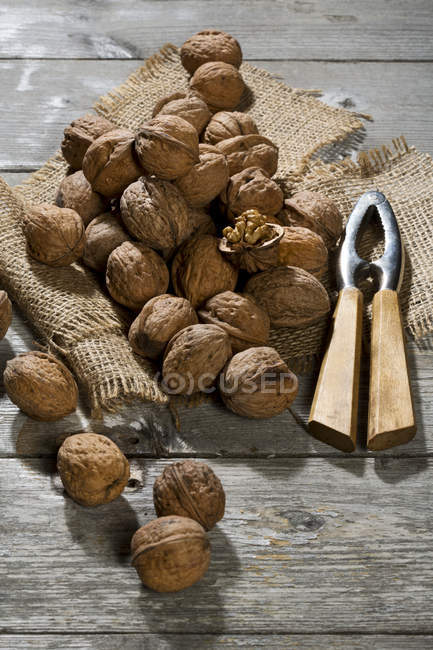 Walnuts (Juglans regia), nutcracker and burlap on wooden table — Stock Photo