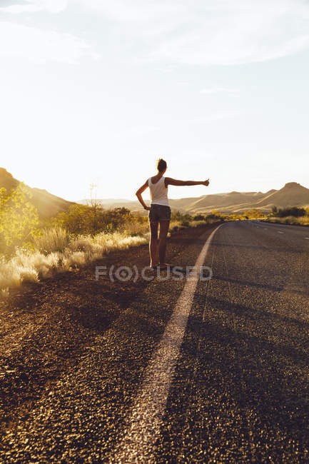 Молодая женщина автостопом по дороге — стоковое фото