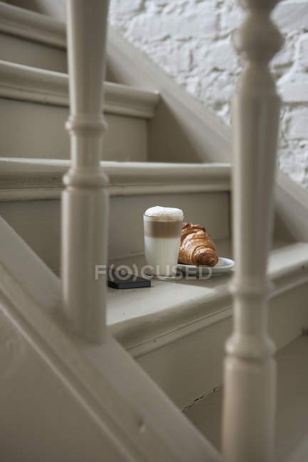Croissant and drink on steps with mobile phone — Stock Photo