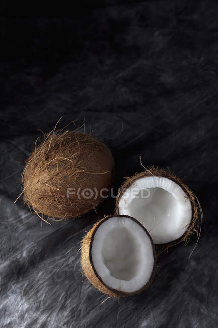 Цельные и наполовину кокосы на черной ткани — стоковое фото