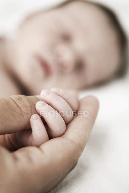 Отец держит за руку спящего новорожденного сына — стоковое фото