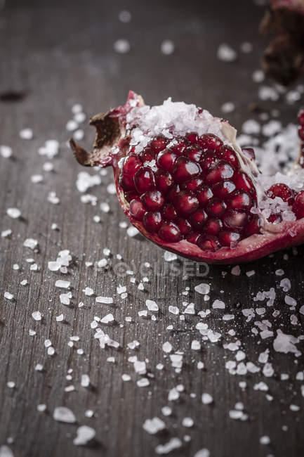 Pedazo de granada fresca con sal marina gruesa sobre madera oscura - foto de stock