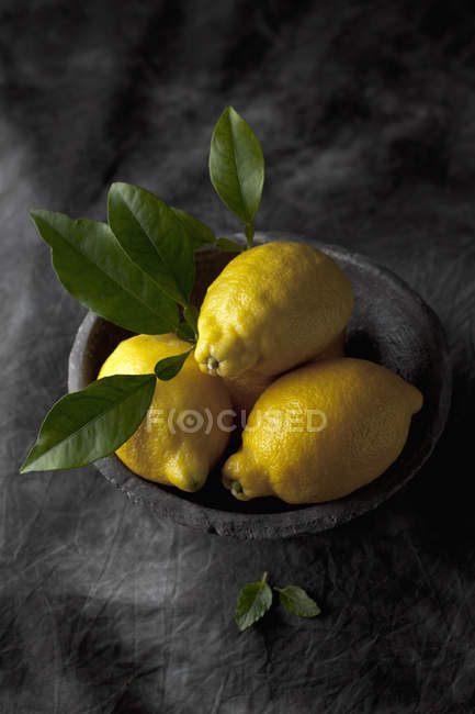 Fresh lemons with leaves in bowl on black fabric — Stock Photo