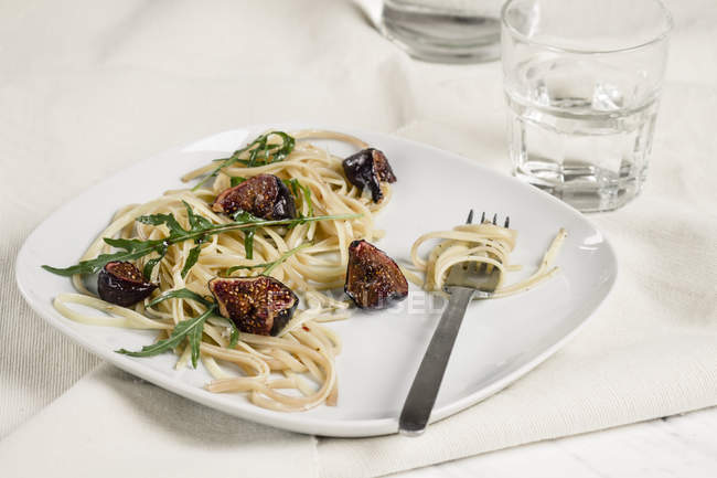 Plate with fig tagliatelle, rocket leaves, sauce and a glass of water, studio shot — Stock Photo
