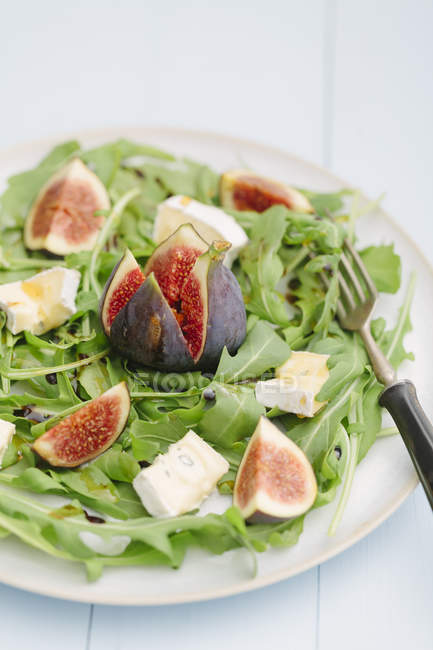 Salad with rocket, figs and Camembert cheese on plate with fork — Stock Photo