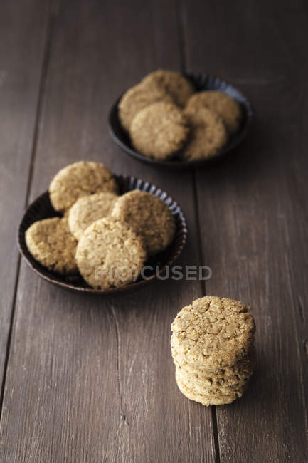 Oat cookies in bowls and on dark wood — Stock Photo