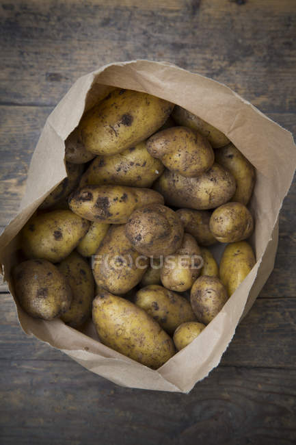 Fresh dirty Potatoes in paper bag on dark wood — Stock Photo