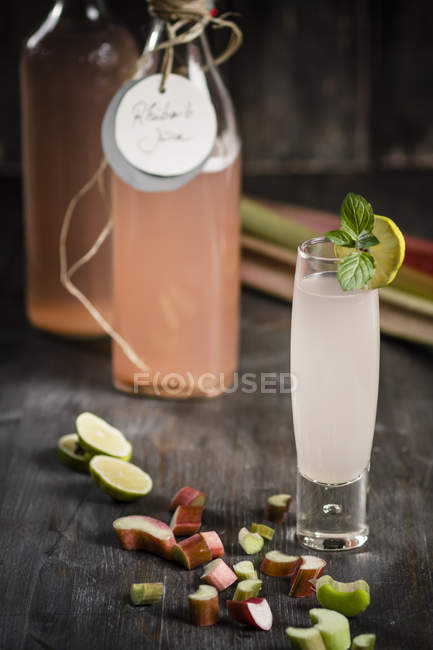 Glass and bottle of rhubarb juice and pieces of rhubarb on wooden surface — Stock Photo