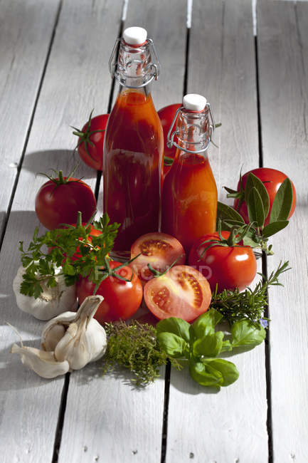 Close-up of two bottles of homemade tomato juice with fresh tomatoes on wooden table — Stock Photo