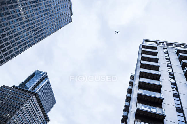 Reino Unido, Londres, Docklands, partes de três edifícios no distrito financeiro e avião no céu acima — Fotografia de Stock