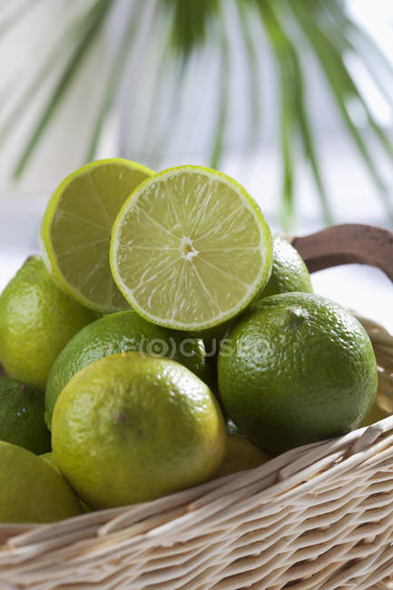Gros plan de citrons verts coupés en deux et entiers dans le panier — Photo de stock