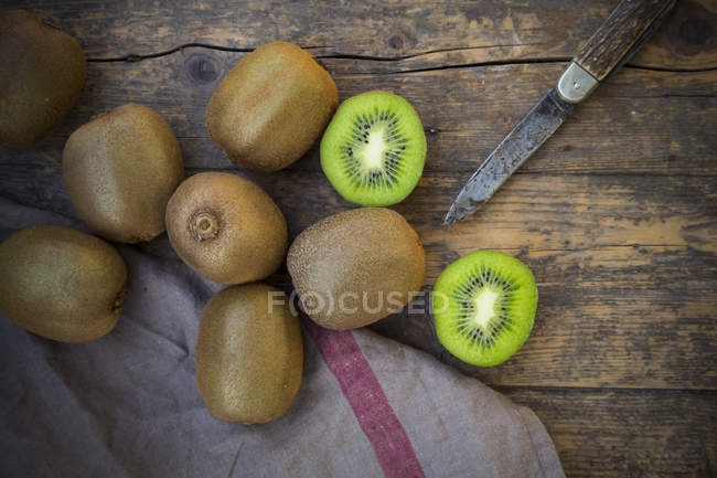 Fresh whole and halved kiwi fruits with knife on dark wood — diet ...