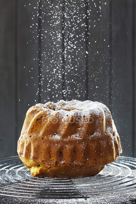 Sprinkling homemade ring cake with powdered sugar on wire rack — Stock Photo
