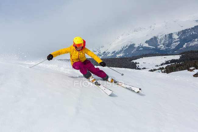 Жінка катається на сніжному гірському схилі в яскравому лижному одязі, шоломі та окулярах — стокове фото