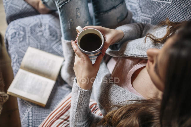 Young woman at home relaxing with cup of coffee and a book — Stock Photo