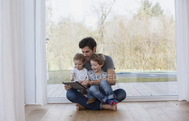 Padre e hijos sentados en el suelo usando tableta digital - foto de stock
