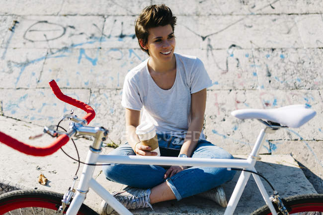 Giovane donna sorridente con bicicletta e caffè per andare — Foto stock