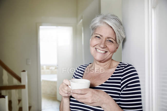 Портрет улыбающейся женщины с чашкой кофе дома — стоковое фото