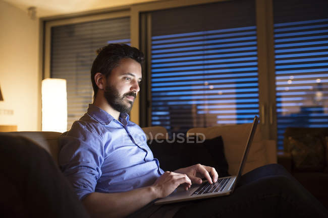 Hombre sentado en el sofá, utilizando el ordenador portátil - foto de stock