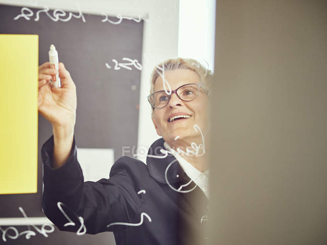 Frau schreibt auf Glasscheibe in Klassenzimmer — Stockfoto