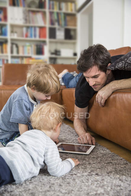 Vater liegt mit Söhnen auf Sofa mit digitalem Tablet — Stockfoto