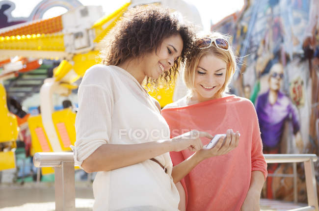 Two young women at fairground using smart phone — Stock Photo