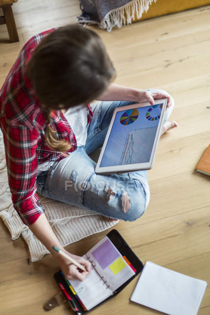 Mujer joven en casa trabajando con tableta digital, tomando notas - foto de stock