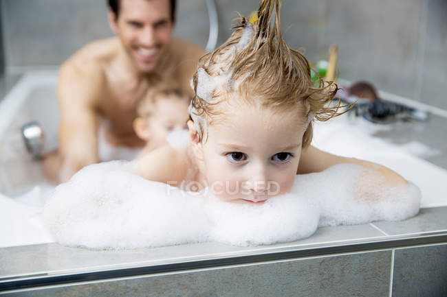 Boy looking pensive with father and little brother in bathtub — Stock Photo