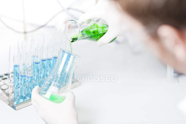 Joven sceintist vertiendo líquido verde en erlenmeyer frasco - foto de stock
